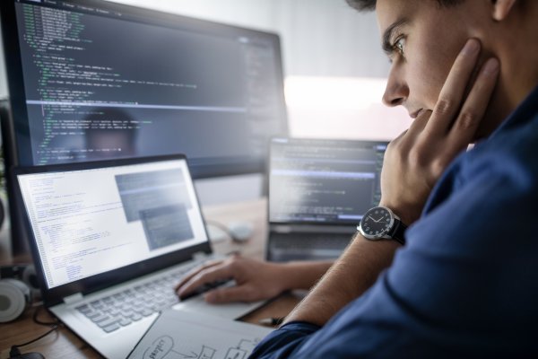 Guy looking at computer code on a screen at a desk.